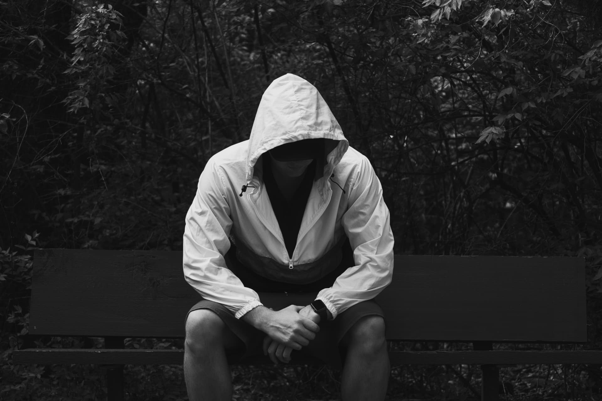 A hooded figure seated alone in quiet surroundings